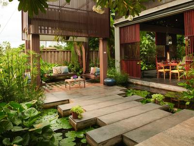 Un'area esterna moderna con un grande passaggio in legno, piante e comodi posti a sedere vicino a una casa.