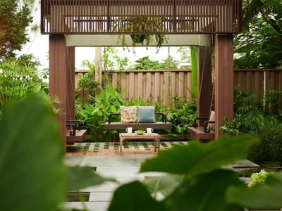 Pohodlná sedací zóna pod dřevěným pavilonem obklopena bujnou zelení a rostlinami.