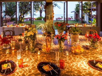 Elegantně osvětlený jídelní stůl s květinovými aranžmá v otevřené restauraci s výhledem na moře.