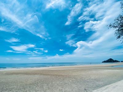 Široká písčitá pláž s jasnou oblohou a několika mraky nad mořem.