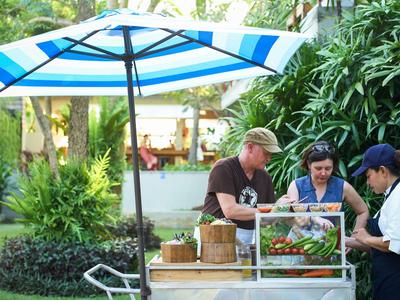 Tre persone e un carretto del cibo sotto un ombrellone blu in un giardino verde.