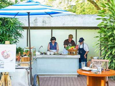 Tre persone preparano cibo a una bancarella all'aperto con un ombrellone.