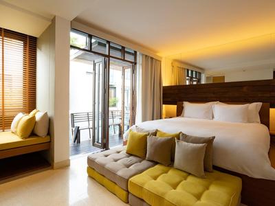 Světý hotelový pokoj s velkou postelí, lavicí a balkonem s výhledem ven.