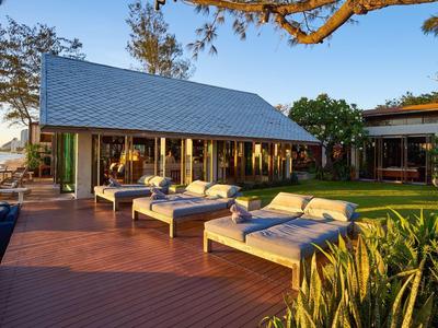 Moderní bungalov s lehátky na dřevěné terase s výhledem na vodu při západu slunce.