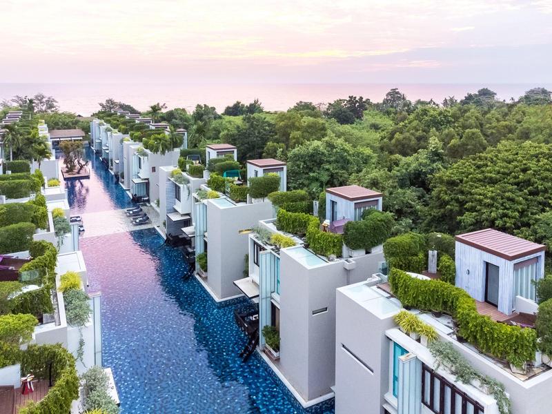 Moderní vily se střechovými terasami obklopují dlouhý bazén u zeleného lesa.