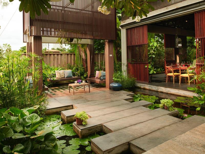 Pohodlná terasa s dřevěnou cestou a posezením obklopená bujnou zelení a rybníkem.