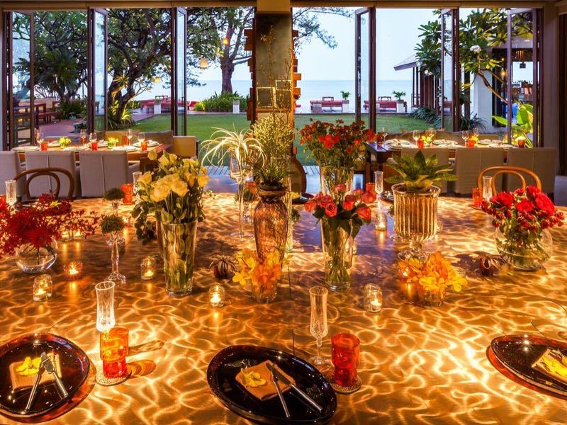 Elegantně osvětlený jídelní stůl s květinovými aranžmá v otevřené restauraci s výhledem na moře.