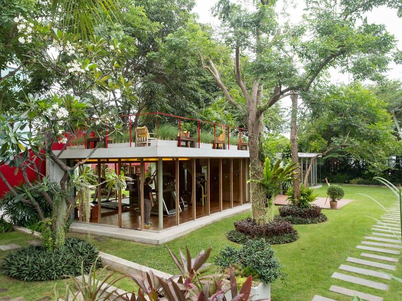 Moderní pavilon se skleněnými stěnami obklopený zelenou zahradou a kamennou cestou.