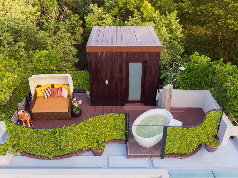 Střešní terasa s útulným posezením, malým bazénem a dřevěnou chatkou obklopenou zelenými keři.