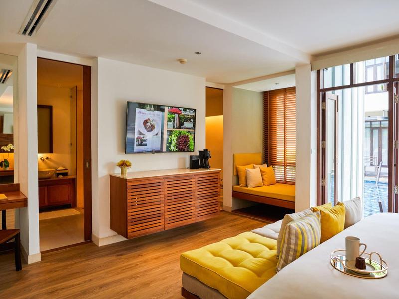 Moderně zařízený hotelový pokoj se žlutou pohovkou a velkým oknem na balkon.