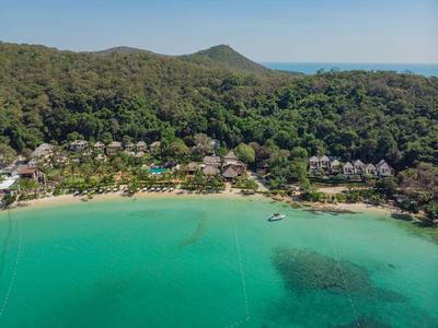 Grüne Bucht mit klarem Wasser, Strand und bewaldeten Hügeln im Hintergrund.