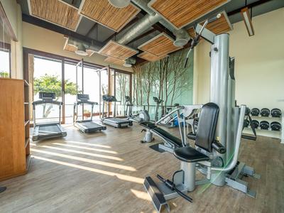 Moderner Fitnessraum mit Trainingsgeräten und Laufbändern, großer Fensterfront und Holzakzenten.