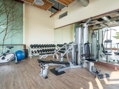 Moderner Fitnessraum mit Trainingsgeräten, Hanteln und großen Fenstern mit Tageslicht.