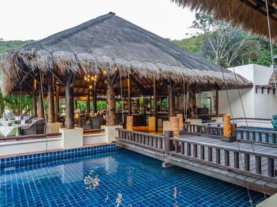Außergewöhnliche Poolbar mit Strohdach und Holzterrasse in tropischer Umgebung.