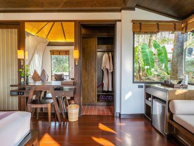 Przytulny pokój hotelowy z drewnianym wystrojem, biurkiem i dużym oknem z widokiem na zieleń.