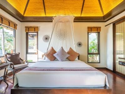 Jasny pokój hotelowy z dużym łóżkiem, moskitierą i przytulnym kącikiem do siedzenia.