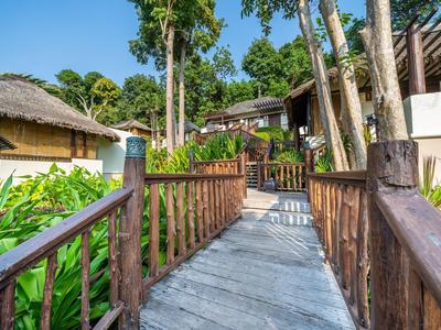 Drewniana ścieżka do bungalowów w tropikalnym hotelu z zielonymi liśćmi i niebieskim niebem.