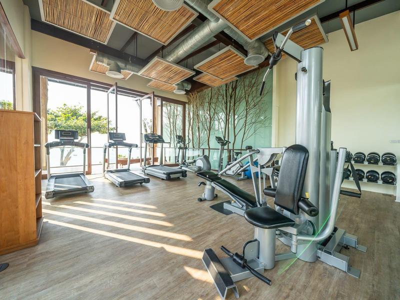 Jasna siłownia z bieżniami, maszyną siłową i hantlami w nowoczesnym otoczeniu.