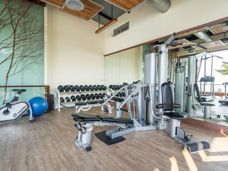 Nowoczesna siłownia z hantlami, sprzętem treningowym i dużymi oknami z widokiem na zewnątrz.