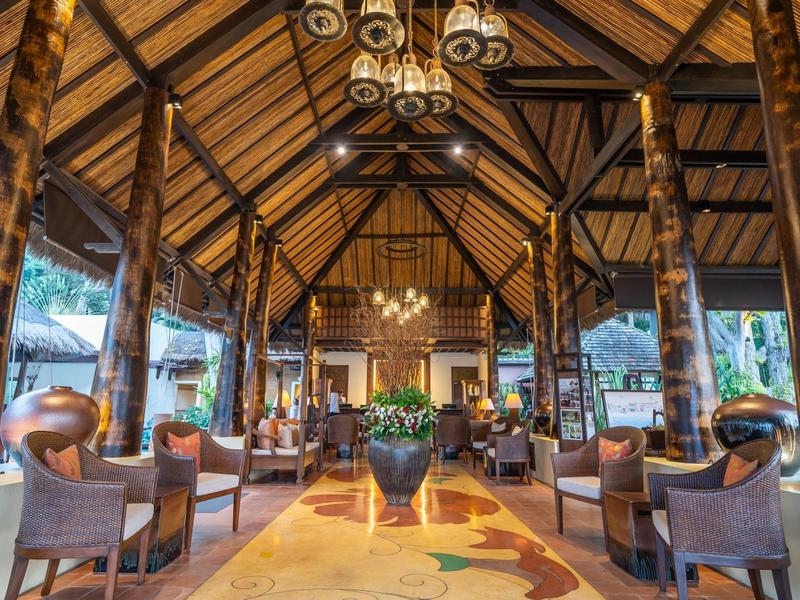 Przestronny salon hotelowy z drewnianymi belkami, żyrandolami i wygodnymi fotelami.