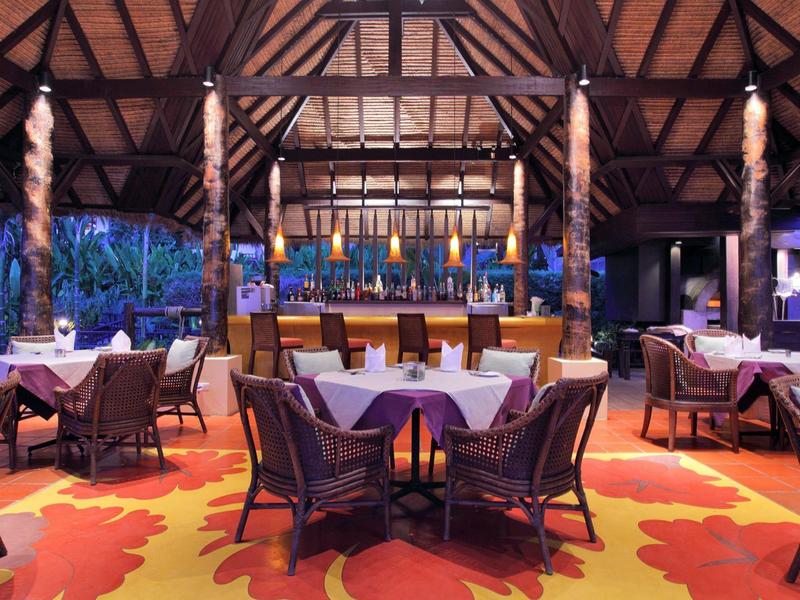 Restauracja na świeżym powietrzu z drewnianymi belkami, kolorowym dywanem i przytulnymi miejscami do siedzenia o zmierzchu.