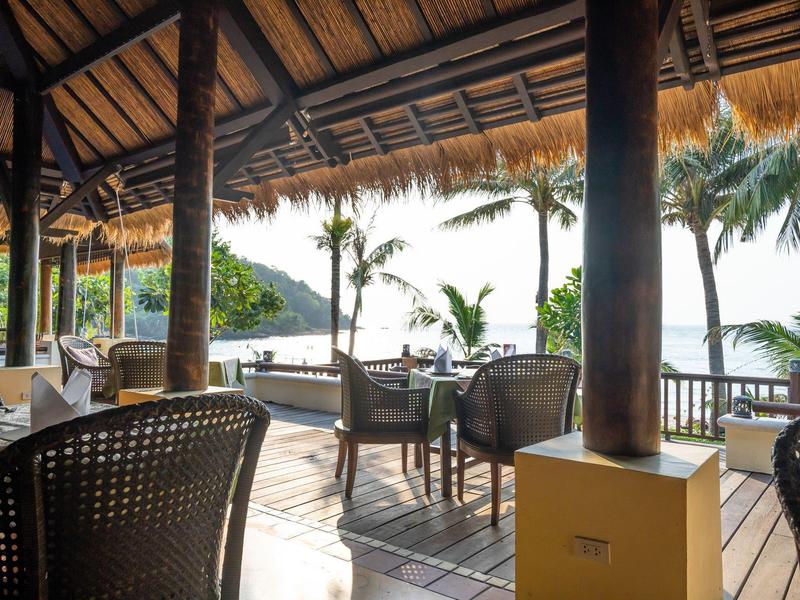 Otwarty teren restauracyjny z widokiem na tropikalne palmy i wodę w tle.