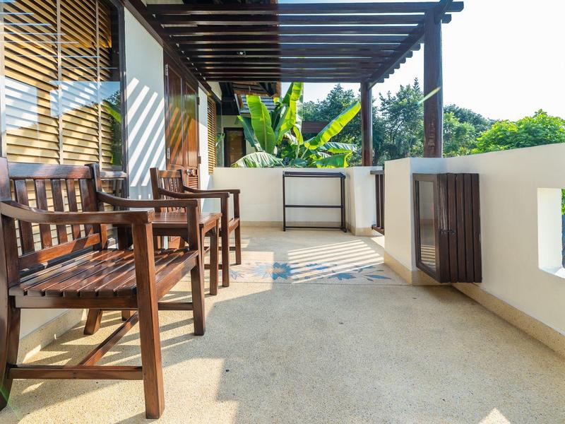 Balkon z drewnianymi krzesłami i pergolą, otoczony białym balustradą i zielenią.