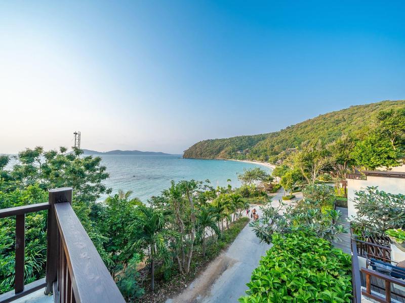 Widok z balkonu na plażę z czystym niebem i zalesionymi wzgórzami.