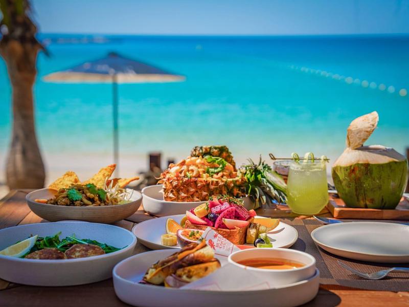 Stół z różnymi potrawami i napojami na plaży z morzem w tle.