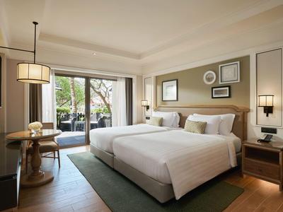 Moderne hotelkamer met twee bedden, bureau, tv en balkon met uitzicht op bomen.