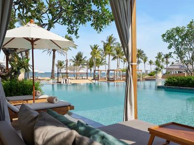 Relaxing pool area with loungers and palm trees by the water under a sunny sky.