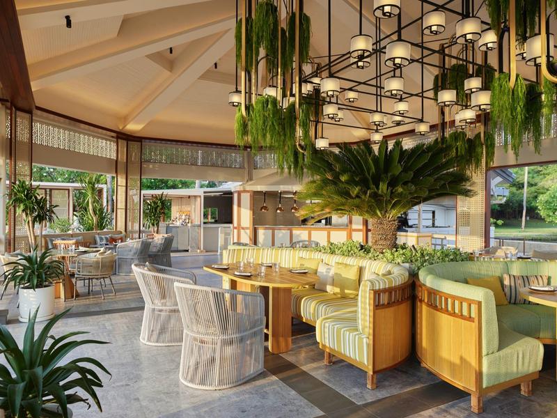 Bright hotel dining area with green chairs and plants, cozy atmosphere with large chandelier.