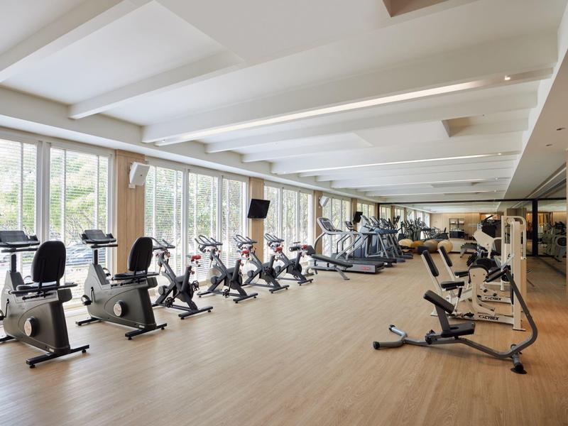 Spacious gym with modern equipment and abundant natural light from large windows.