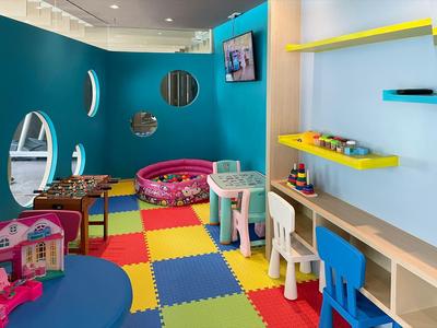 Area giochi colorata per bambini con tappeto puzzle, giocattoli e tavoli in hotel.