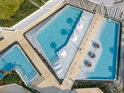 Drei geometrisch geformte Außenpools mit Liegestühlen und Sonnenschirmen am Rand.