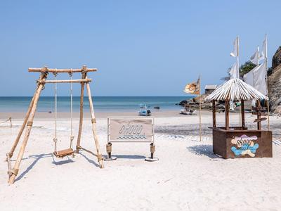 Spiaggia di sabbia vuota con altalena, panchina e piccolo chiosco in una giornata di sole.