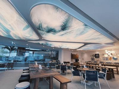 Modernes Hotelrestaurant mit großen Fenstern und künstlerischer Beleuchtung an der Decke.