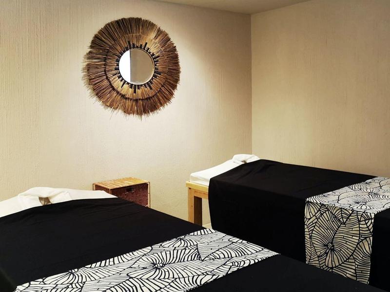 Sala trattamento con due lettini da massaggio, coperture nere e specchio rotondo.