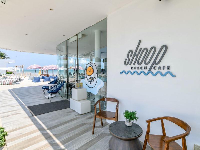 Moderno beach café con vetrata, sedie in legno e vista sulla spiaggia e sul mare.