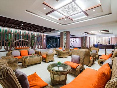 Ampia zona lounge in hotel con mobili in vimini e cuscini arancioni.