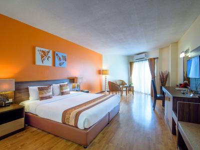 Světý hotelový pokoj s manželskou postelí, oranžovou zdí, psacím stolem a televizí