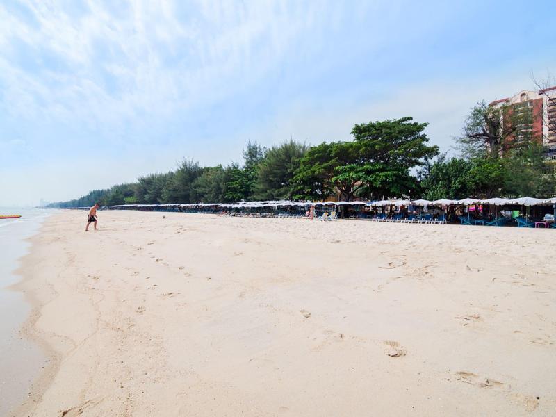 Široká písečná pláž s rozptýlenými lidmi a řadou stromů u moře.