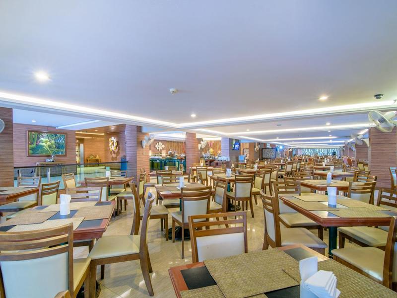 Světla a prostorná restaurace s mnoha dřevěnými stoly a židlemi, moderní osvětlení.