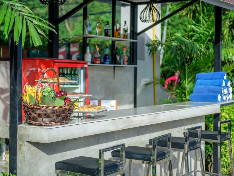 Moderní venkovní bar s betonovým barem, černými stoličkami a tropickou zelení.