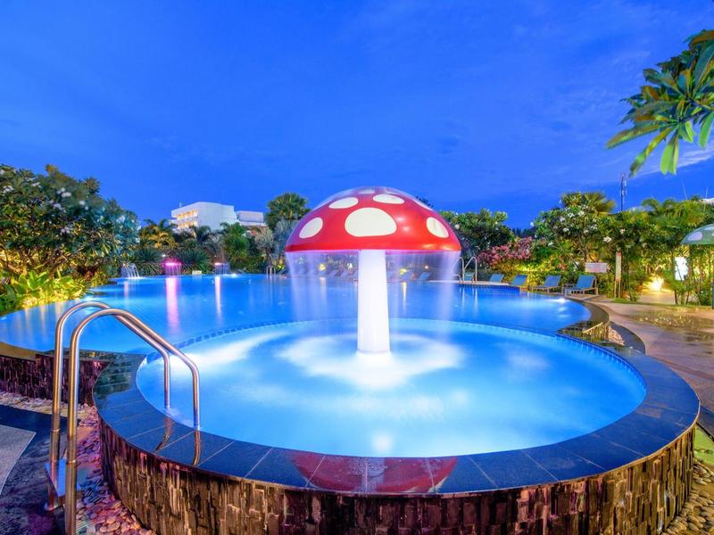 Osvětlený bazén se zvířecí fontánou ve tvaru houby v tropické hotelové zahradě za soumraku