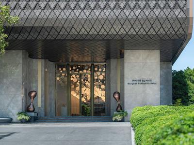 Eingang zu einem modernen Hotel mit Glas- und Metallfassade und grüner Umgebungsbepflanzung.