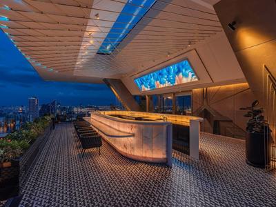 Modern illuminated outdoor bar area with seating on a rooftop terrace at night.