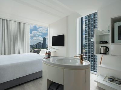 Modern hotel room with large bed, sink, and city view through window.