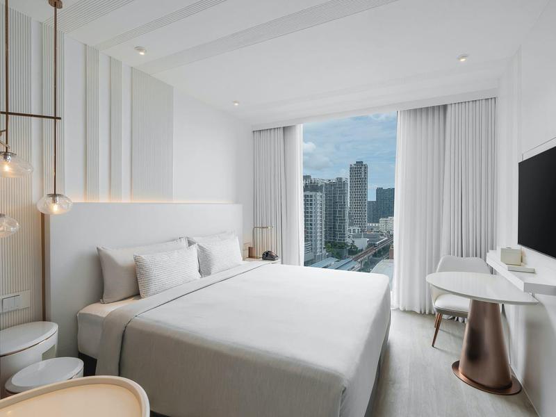 Modern hotel room with large bed and city view through floor-to-ceiling windows.