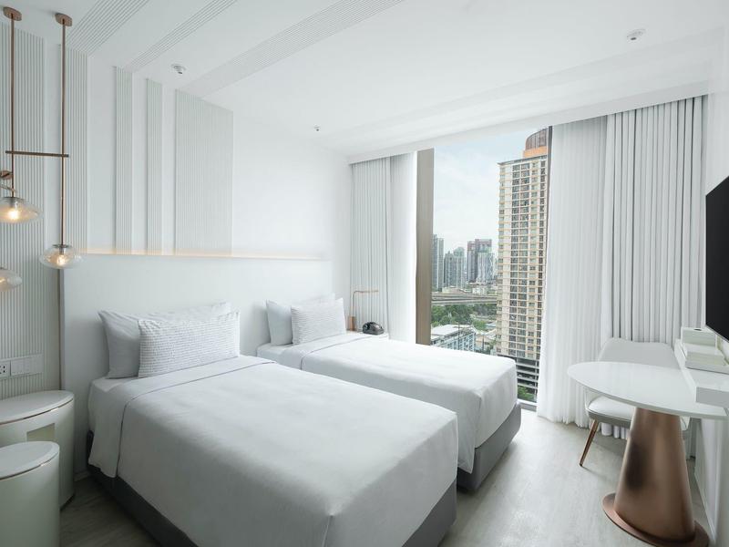 Modern hotel room with two single beds, large windows, and city view.